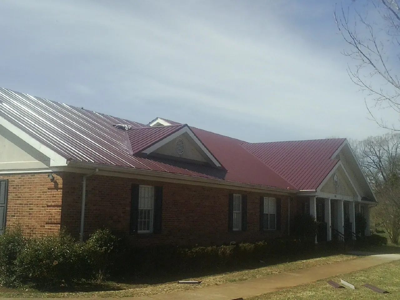 Red metal roof with gabled entries on a long brick building, from a Hail Damage Roof Repair job in Churchton