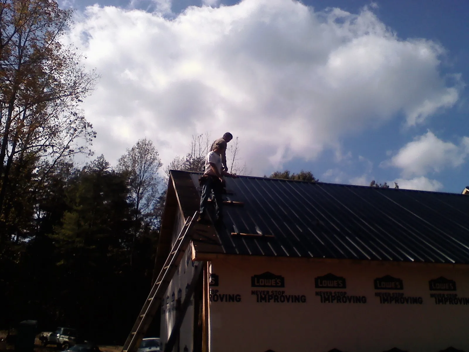 Roofer fastening dark metal panels high against a cloudy sky, from a Roof Inspection job in Churchton