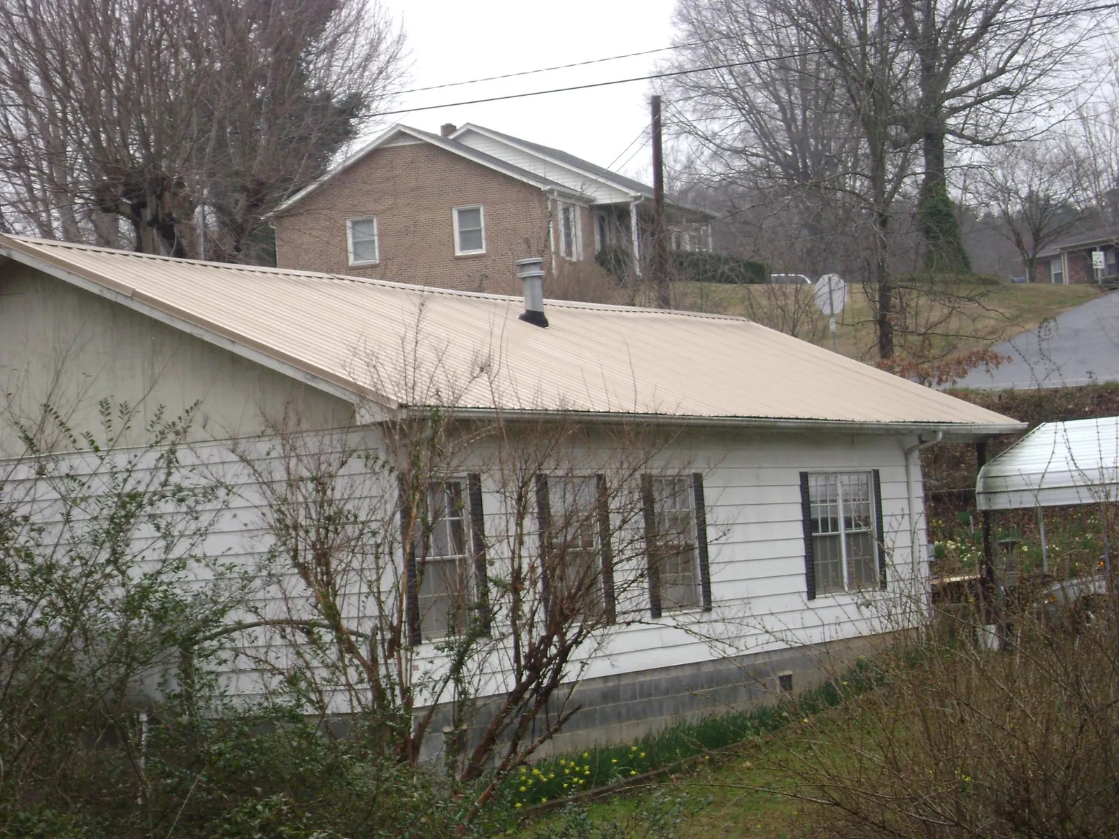 Tan metal roof on a white sided house set into a hillside — Commercial Roofing by Roofing Brothers in Churchton